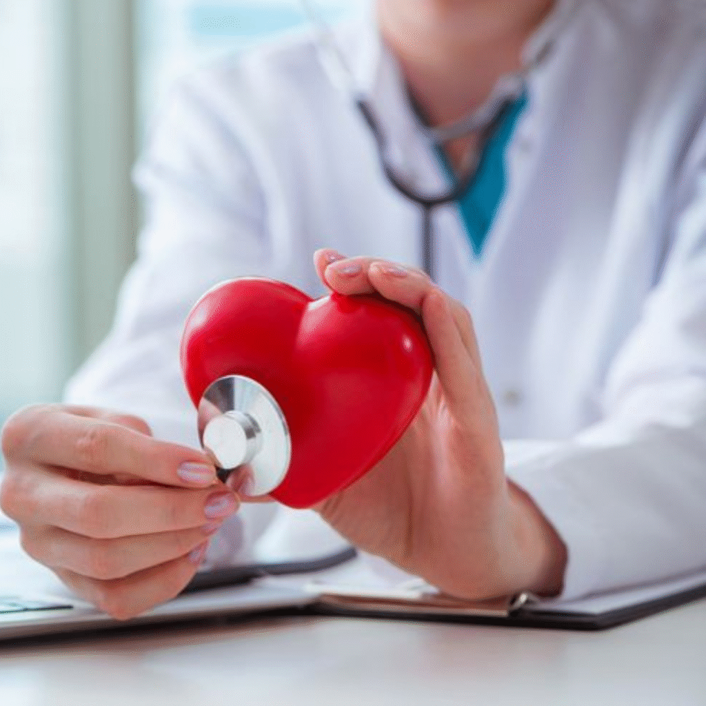 Dr. Jai Bhagwan Dhull performing a heart health checkup using a stethoscope on a red heart model symbolizing expert cardiac cared and cardiovascular wellness.