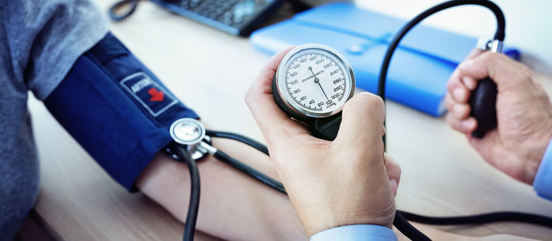 A healthcare professional checks a patient's blood pressure using a manual sphygmomanometer and stethoscope during a medical examination.