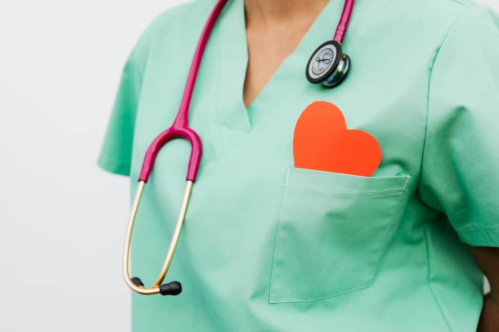A healthcare professional in green scrubs with a red stethoscope and a heart-shaped card in the pocket, symbolizing compassionate medical care — representing Doctor Jai Bhagwan Dhull's dedication to patient wellness.