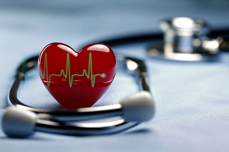 A red heart model displaying an electrocardiogram (ECG) line is placed within a stethoscope on a blue medical cloth, symbolizing heart health and cardiac monitoring.