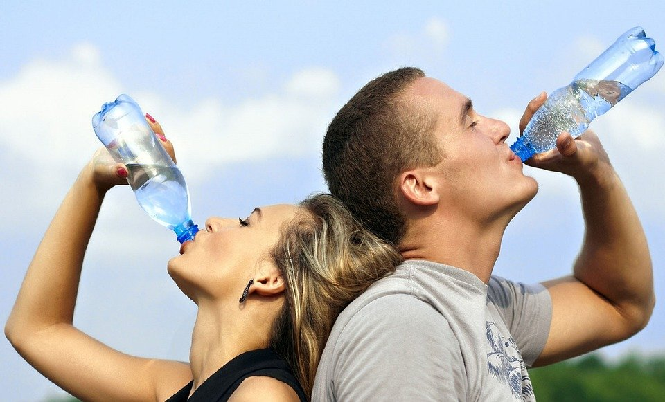 Young couple drinking water from bottles to stay hydrated, promoting healthy lifestyle tips by Dr. Jai Bhagwan Dhull.