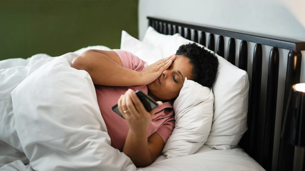 Woman lying in bed feeling tired while holding a phone — Dr. Jai Bhagwan Dhull emphasizes the impact of poor sleep on heart health and overall well-being.