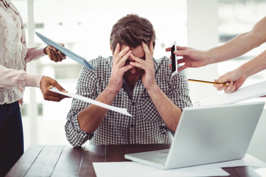 Stressed man at work surrounded by multiple tasks and distractions, feeling overwhelmed by workload.