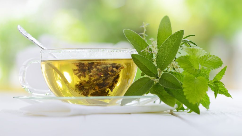 Glass cup of freshly brewed green herbal tea with mint leaves placed beside it, symbolizing natural wellness and healthy lifestyle guidance by Dr. Jai Bhagwan Dhull.
