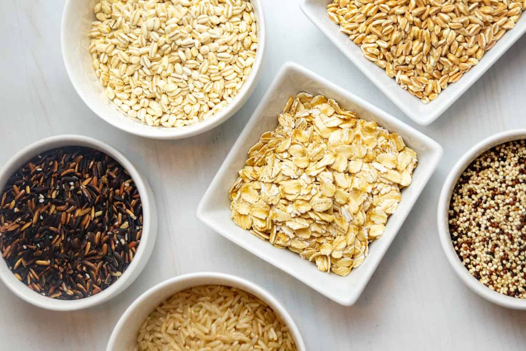 Assorted whole grains including oats, quinoa, barley, wild rice, and brown rice in bowls — a nutritious selection often highlighted by Dr. Jai Bhagwan Dhull for balanced and healthy eating.