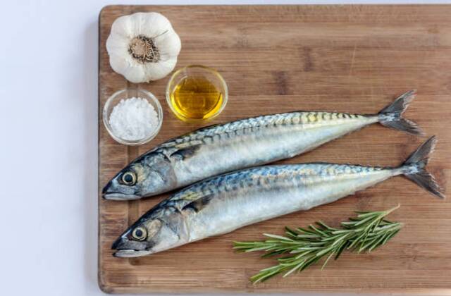 Two fresh mackerel fish placed on a wooden board with garlic, olive oil, sea salt, and rosemary sprigs — a healthy cooking preparation style often recommended by Dr. Jai Bhagwan Dhull for nutritious meals.