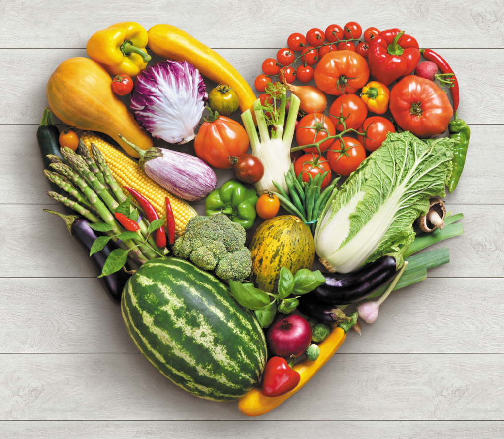 Colorful assortment of fresh fruits and vegetables arranged in the shape of a heart on a wooden background, symbolizing healthy eating and heart wellness.