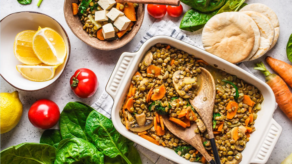 Nutritious selection of heart-healthy foods including salmon fillets, kale, avocado, eggs, almonds, pumpkin seeds, and green vegetables displayed on a light blue background.