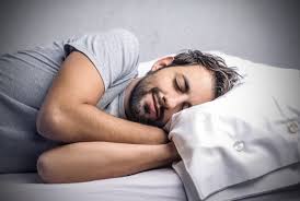 Young man sleeping peacefully on a white pillow, highlighting the importance of healthy sleep patterns for overall well-being, with health insights from Dr. Jai Bhagwan Dhull.