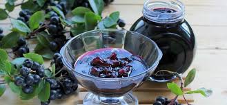 A glass bowl and jar filled with dark berry jam made from fresh chokeberries, placed alongside green leaves and branches — a superfood often recommended by Dr. Jai Bhagwan Dhull for boosting immunity and overall wellness.