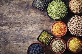 Assorted bowls of colorful lentils and pulses including green gram, red lentils, chickpeas, and black beans placed on a rustic wooden table, representing healthy nutrition and diet awareness promoted by Dr. Jai Bhagwan Dhull."