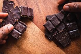Close-up of hands holding pieces of dark chocolate bars placed on a wooden surface, highlighting the importance of mindful eating and nutrition awareness as emphasized by Dr. Jai Bhagwan Dhull.