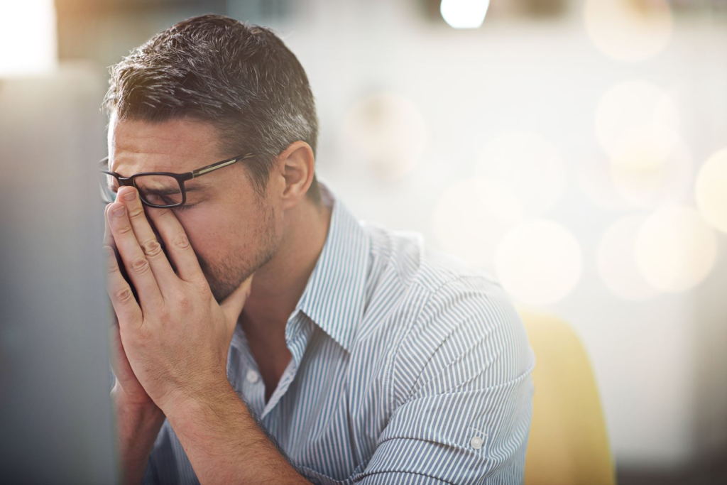 A stressed man sitting at his desk with his hands covering his face, appearing tired or overwhelmed, symbolizing work-related stress and mental fatigue — concept related to stress management and mental wellness awareness by Dr. Jai Bhagwan Dhull.